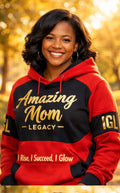 Woman wearing a red and black hoodie with 'Amazing Mom Legacy' text, standing outdoors with blurred foliage in the background.