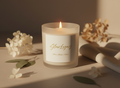 Candle with a 'Glow Legacy' label on a surface with flowers and a blurred background