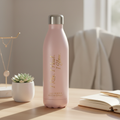 Pink water bottle with text on a table with a plant and book in the background
